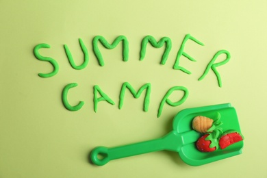 Flat lay composition with words SUMMER CAMP made from modelling clay and plastic shovel on color background