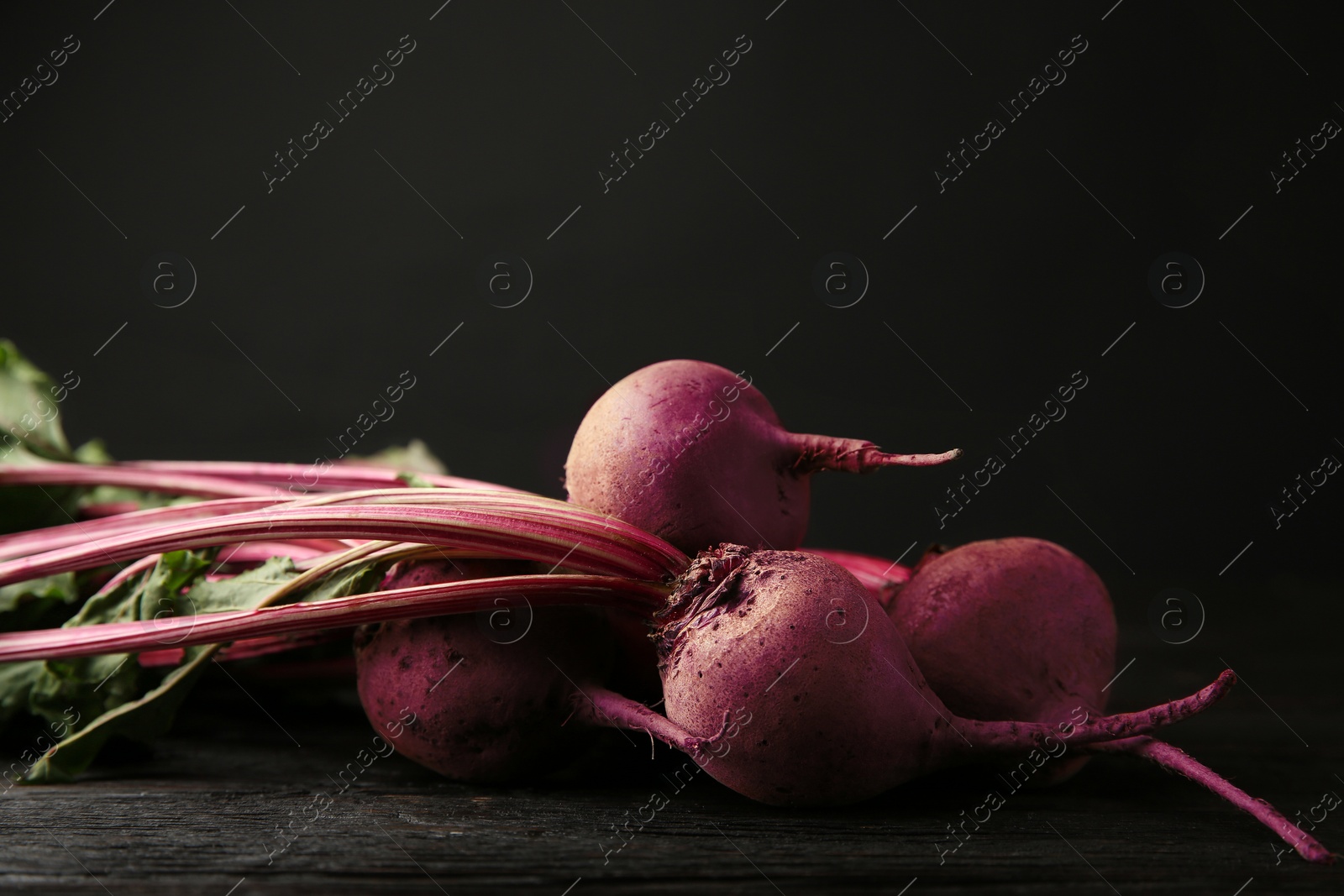 Photo of Fresh beets on dark wooden table against black background. Space for text