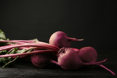 Fresh beets on dark wooden table against black background. Space for text