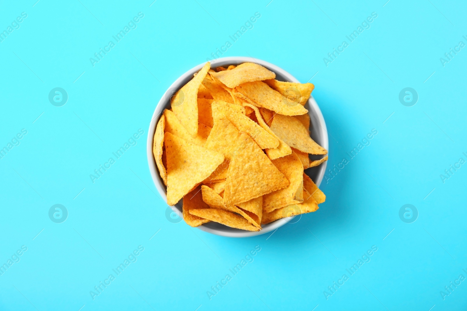 Photo of Tasty mexican nachos chips in bowl on blue background, top view