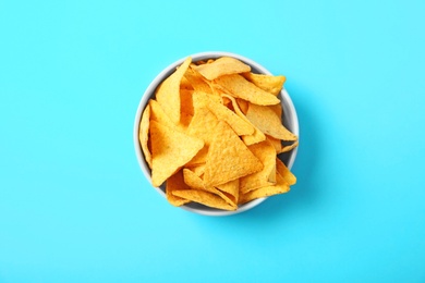 Tasty mexican nachos chips in bowl on blue background, top view