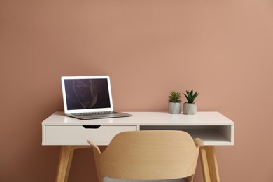 Photo of Stylish workplace with laptop and comfortable chair on beige background. Interior design