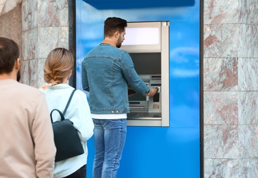 Photo of Young people standing in queue to cash machine outdoors