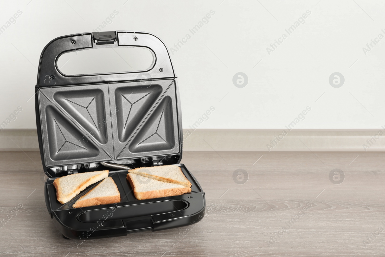 Photo of Modern sandwich maker with bread slices on wooden table near white wall, space for text