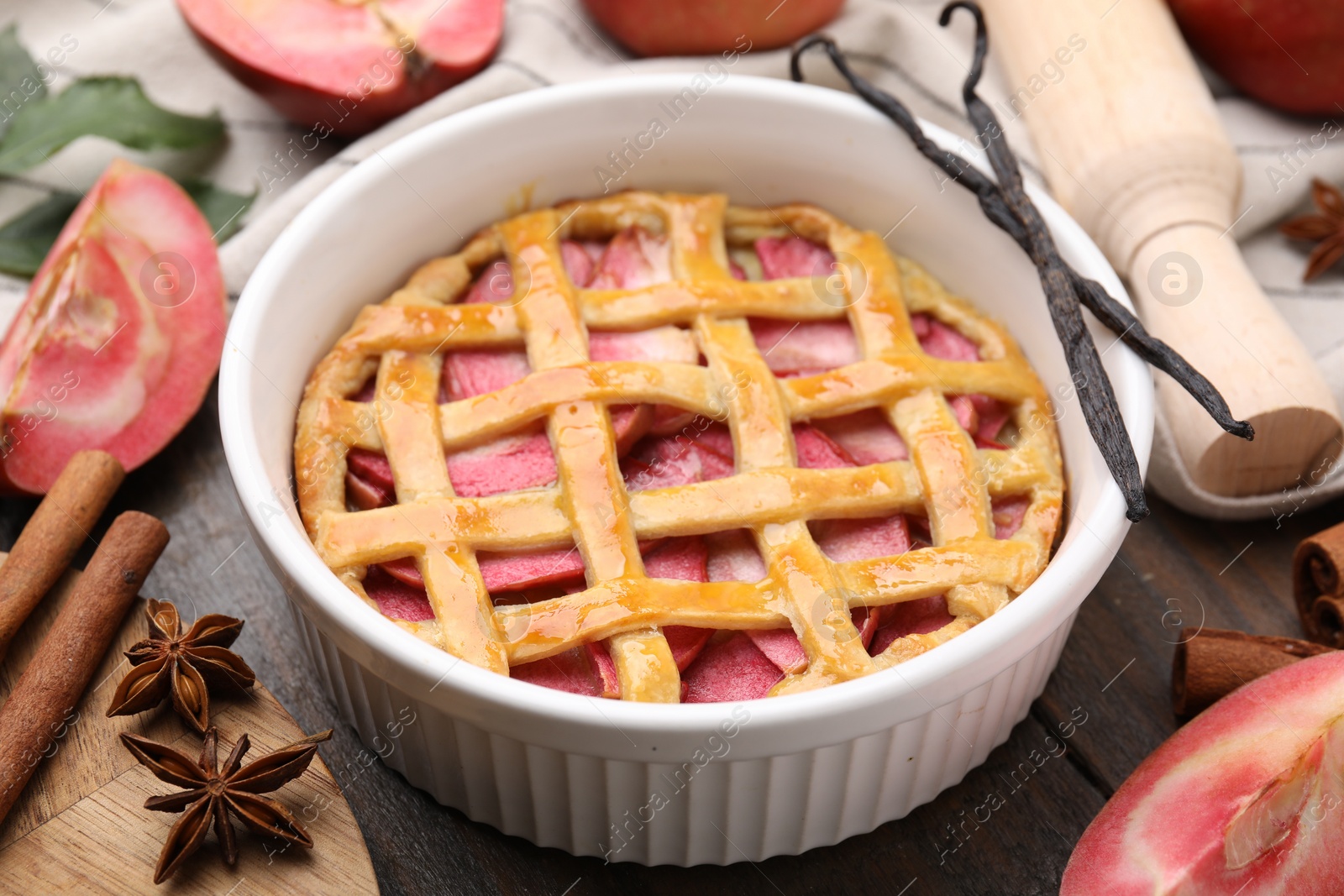Photo of Baking dish with tasty apple pie and spices on wooden table, closeup