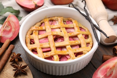 Baking dish with tasty apple pie and spices on wooden table, closeup