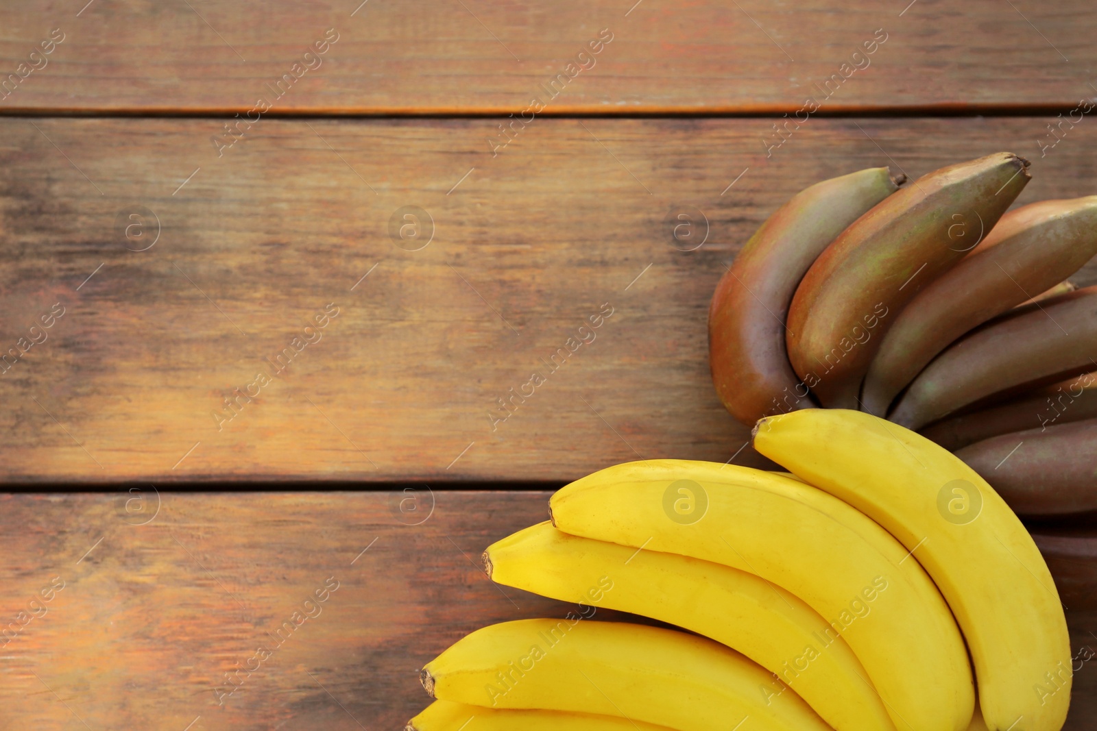 Photo of Tasty purple and yellow bananas on wooden table, above view. Space for text