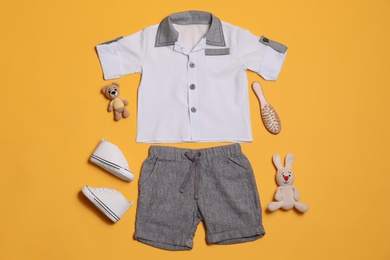 Flat lay composition with baby clothes and toys on yellow background