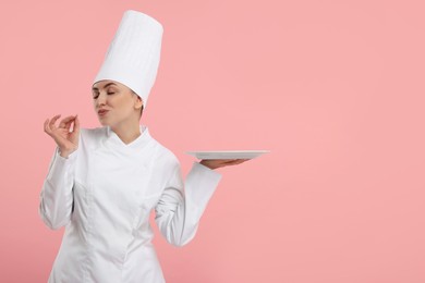 Photo of Happy professional confectioner in uniform holding empty plate on pink background. Space for text