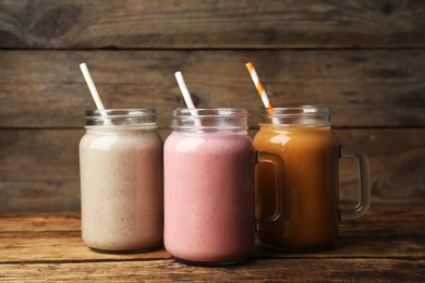 Photo of Mason jars with different tasty smoothies on wooden table