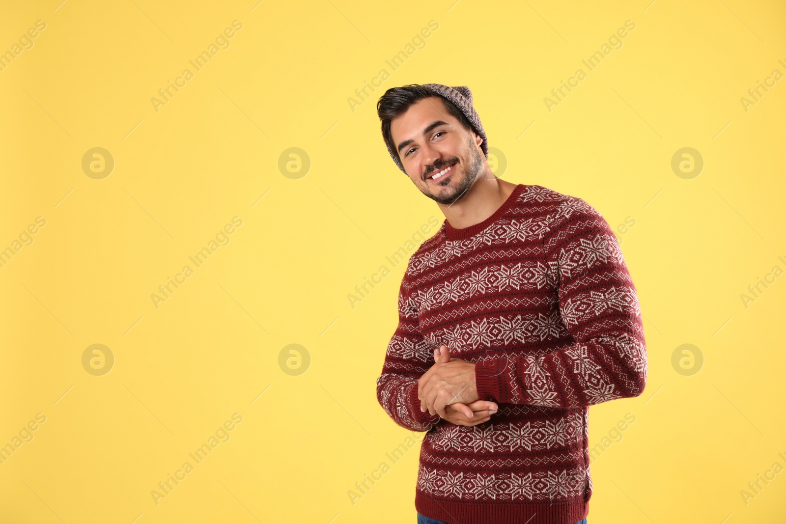 Photo of Portrait of young man in Christmas sweater and hat on yellow background. Space for text