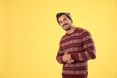 Portrait of young man in Christmas sweater and hat on yellow background. Space for text