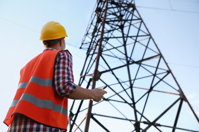 Photo of Electrical engineer with walkie talkie near high voltage tower, low angle view