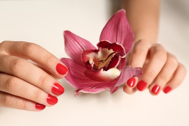 Photo of Woman with red manicure holding flower on white background, closeup. Nail polish trends