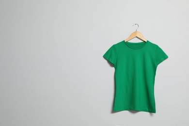 Photo of Hanger with green t-shirt on light wall. Mockup for design