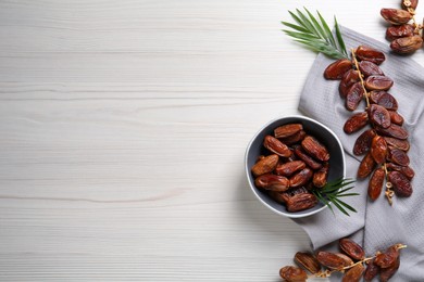 Tasty sweet dried dates with green leaves on white wooden table, flat lay. Space for text