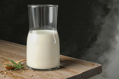 Photo of Composition with glassware of hemp milk on wooden table against dark background. Space for text