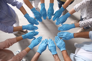 Photo of People in blue medical gloves joining hands indoors, top view