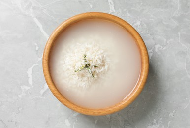 Photo of Bowl with rice soaked in water on light grey marble table, top view