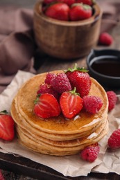 Tasty pancakes with fresh berries and honey on wooden board, closeup