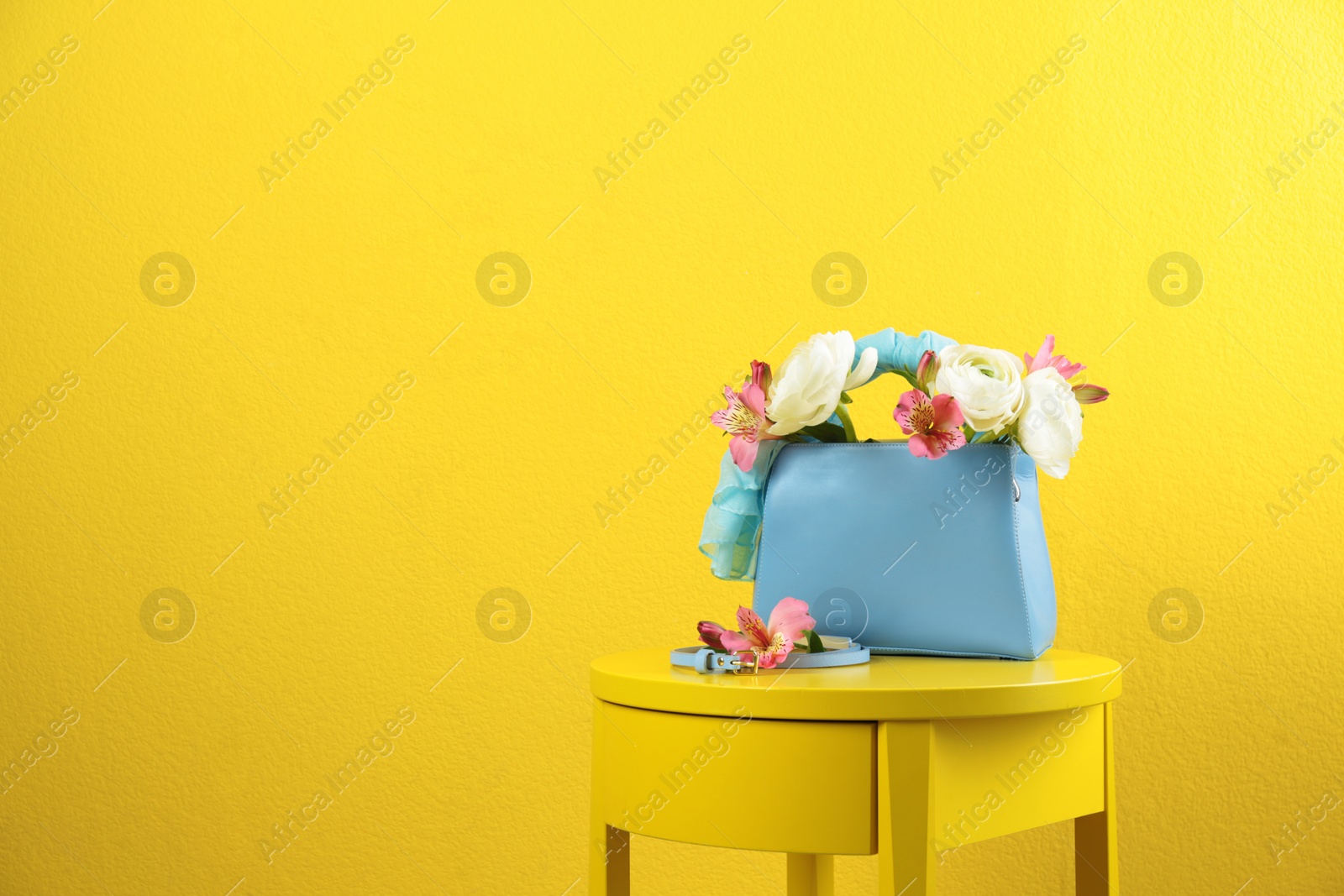 Photo of Elegant handbag with flowers and belt on table against yellow background, space for text