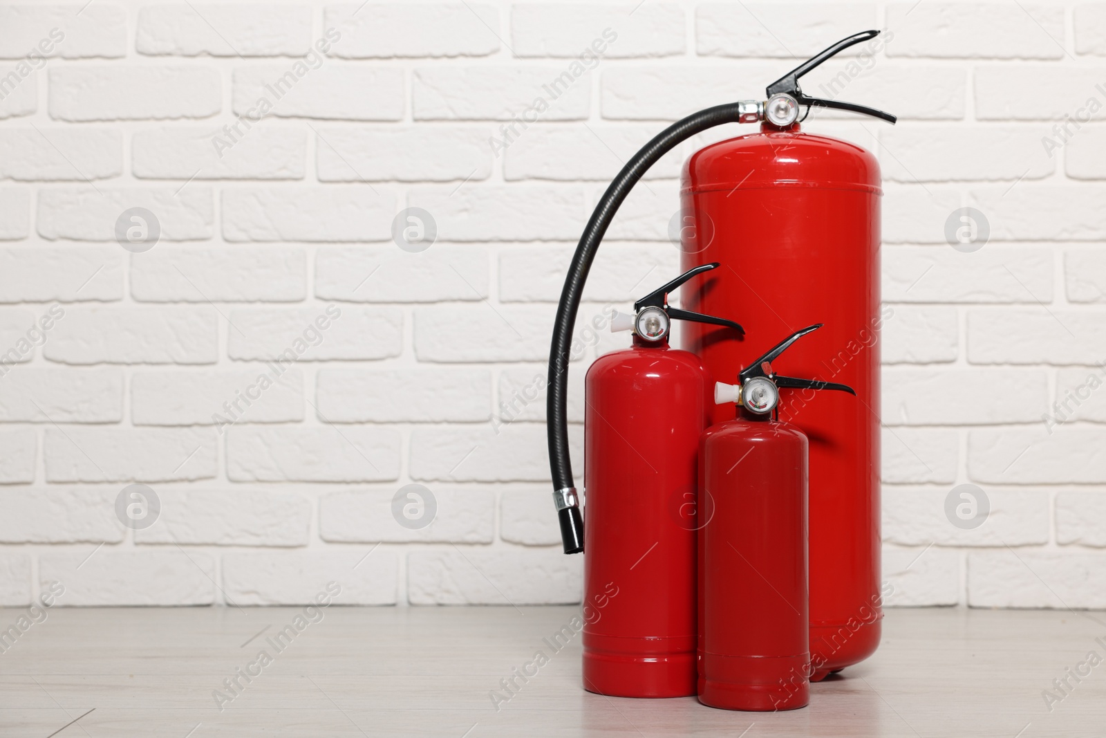 Photo of Red fire extinguishers near white brick wall, space for text