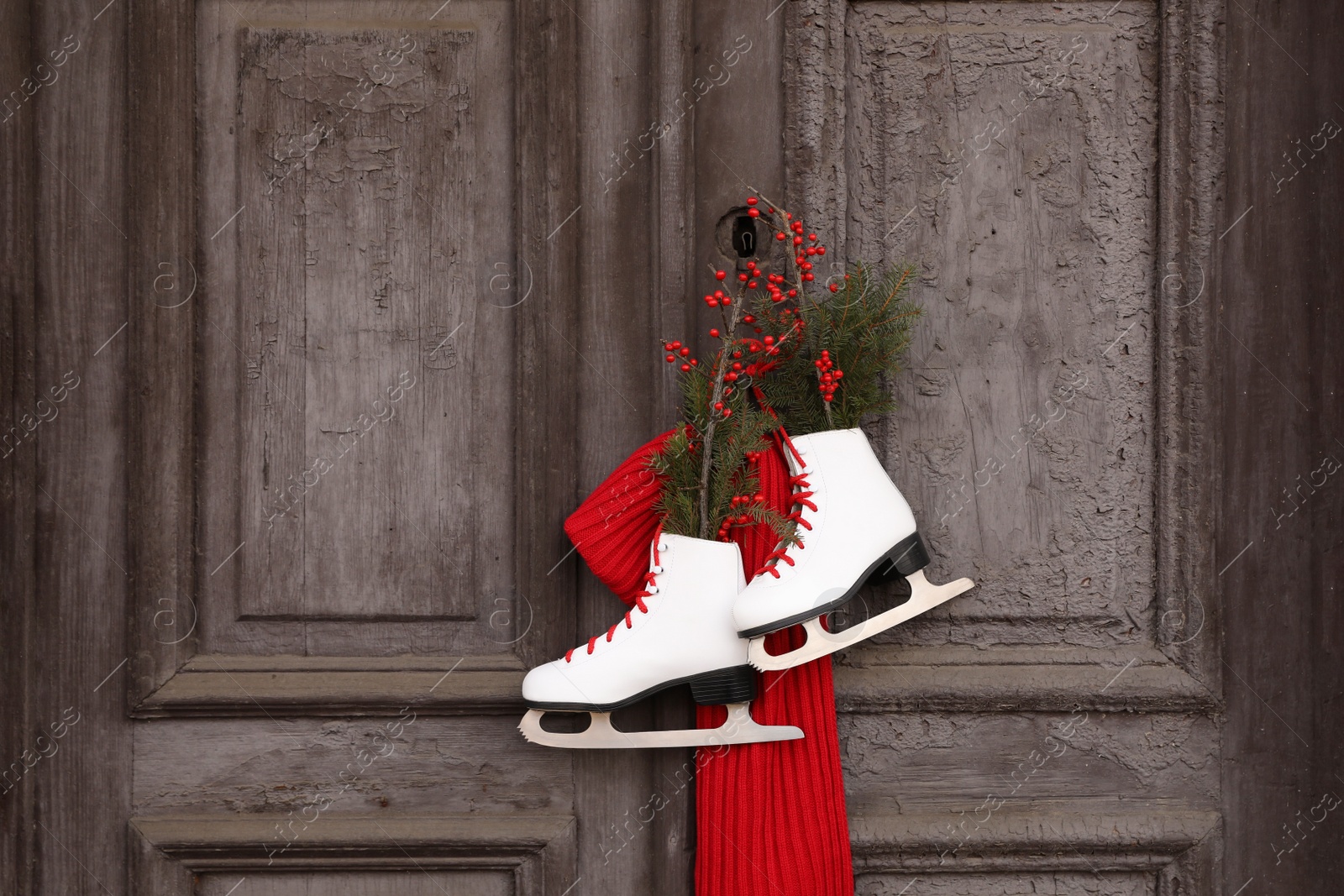 Photo of Pair of ice skates with Christmas decor hanging on old wooden door