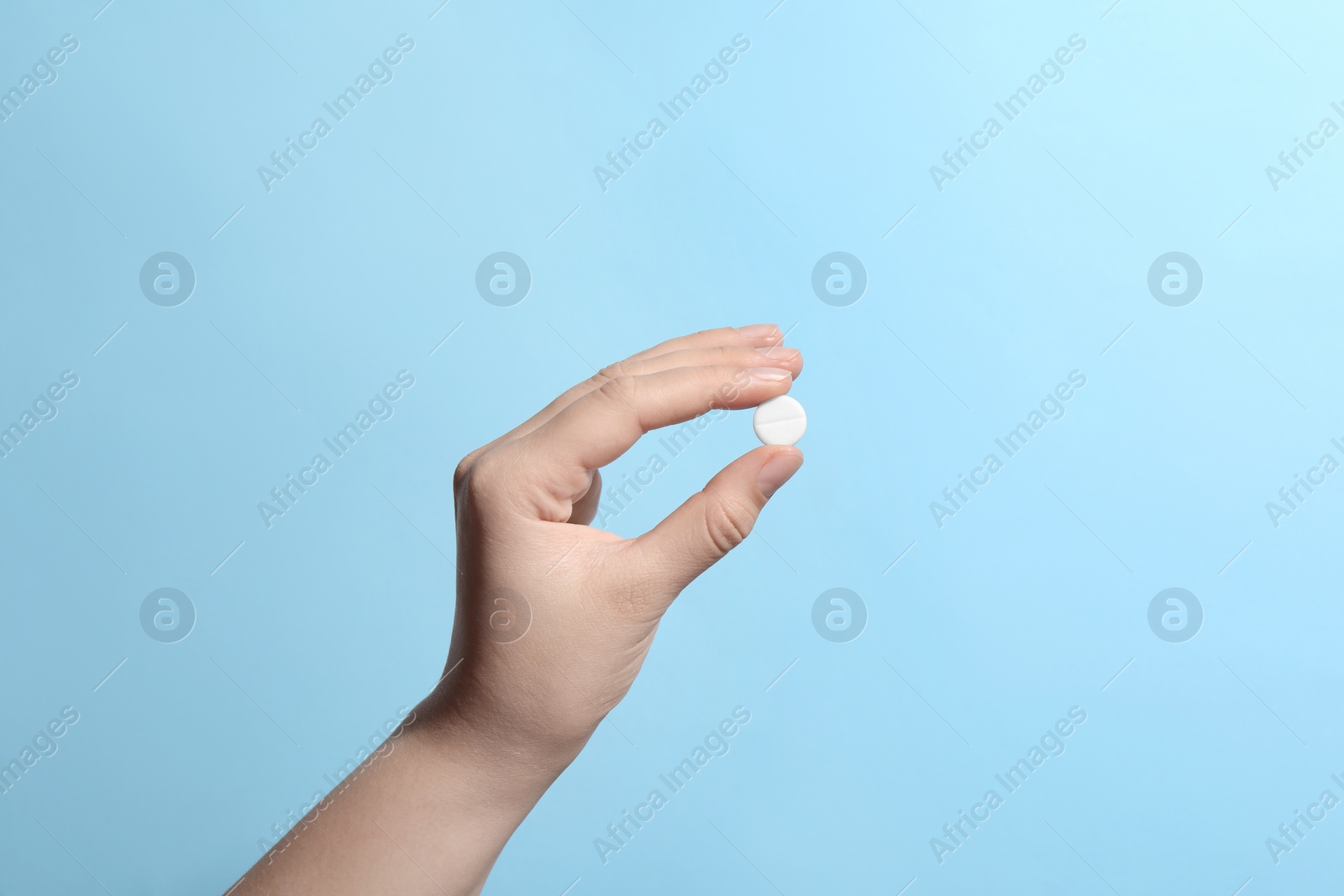 Photo of Woman holding pill on light blue background, closeup