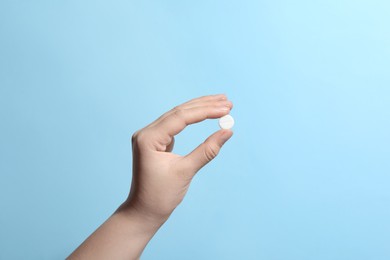 Photo of Woman holding pill on light blue background, closeup