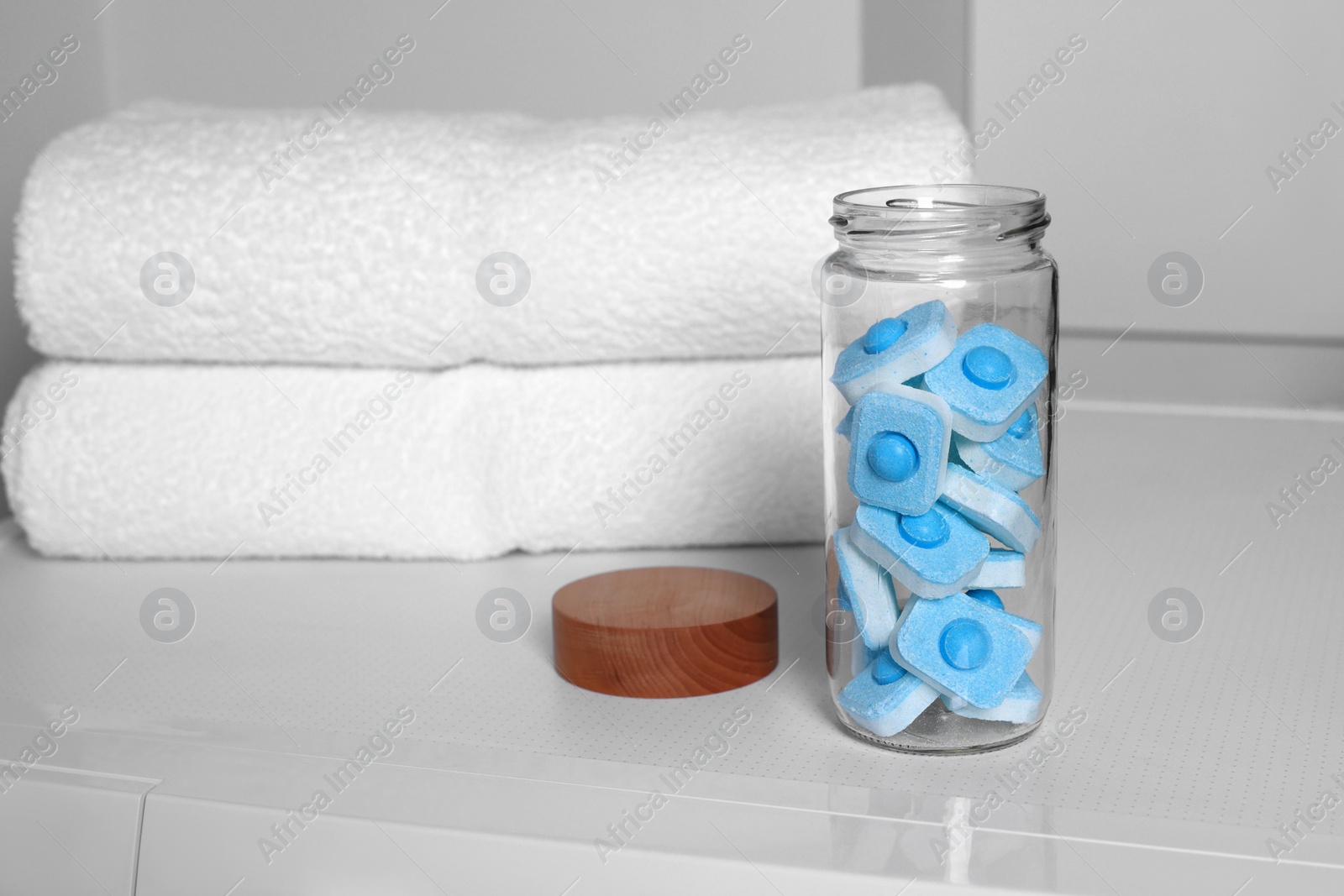 Photo of Glass jar with water softener tablets on washing machine in bathroom, space for text