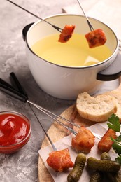 Photo of Fondue pot, forks with fried meat pieces, ketchup and other products on grey textured table