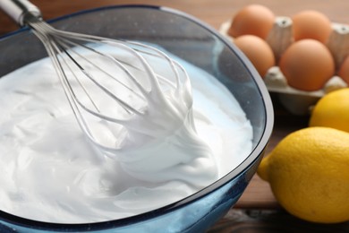 Bowl with whipped cream, whisk and ingredients on table, closeup