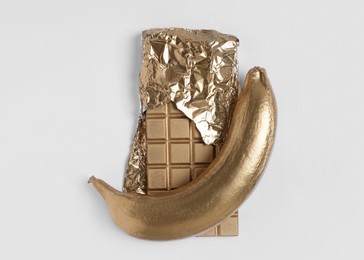 Photo of Shiny stylish golden banana and chocolate bar on white background, top view. Decor elements