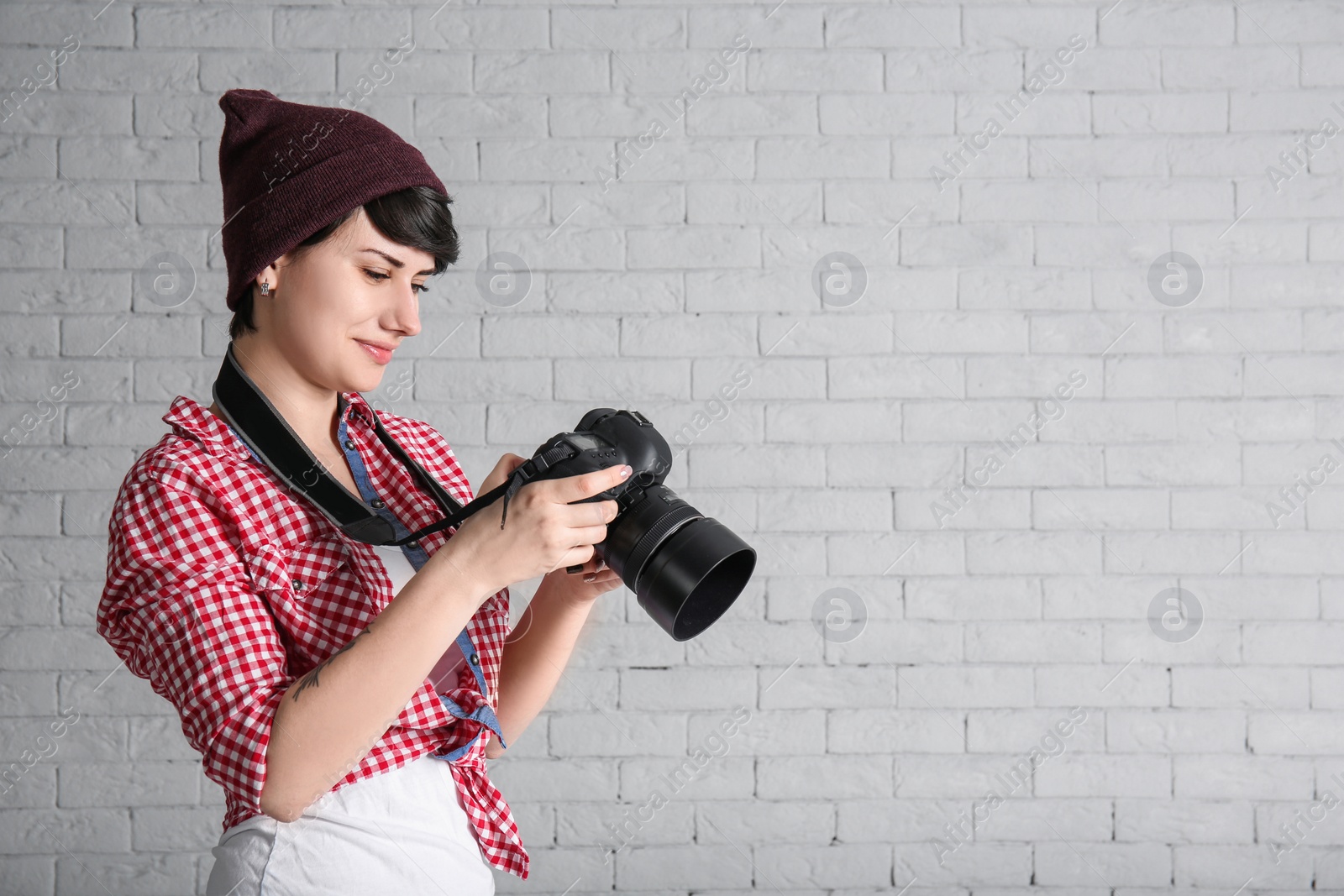 Photo of Young female photographer with camera on brick background