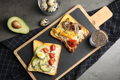 Photo of Different toasts with avocado, mushrooms, cherry tomatoes and chia seeds served on grey table, top view