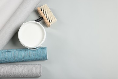 Photo of Different wallpaper rolls, brush and bucket with glue on light background, flat lay. Space for text