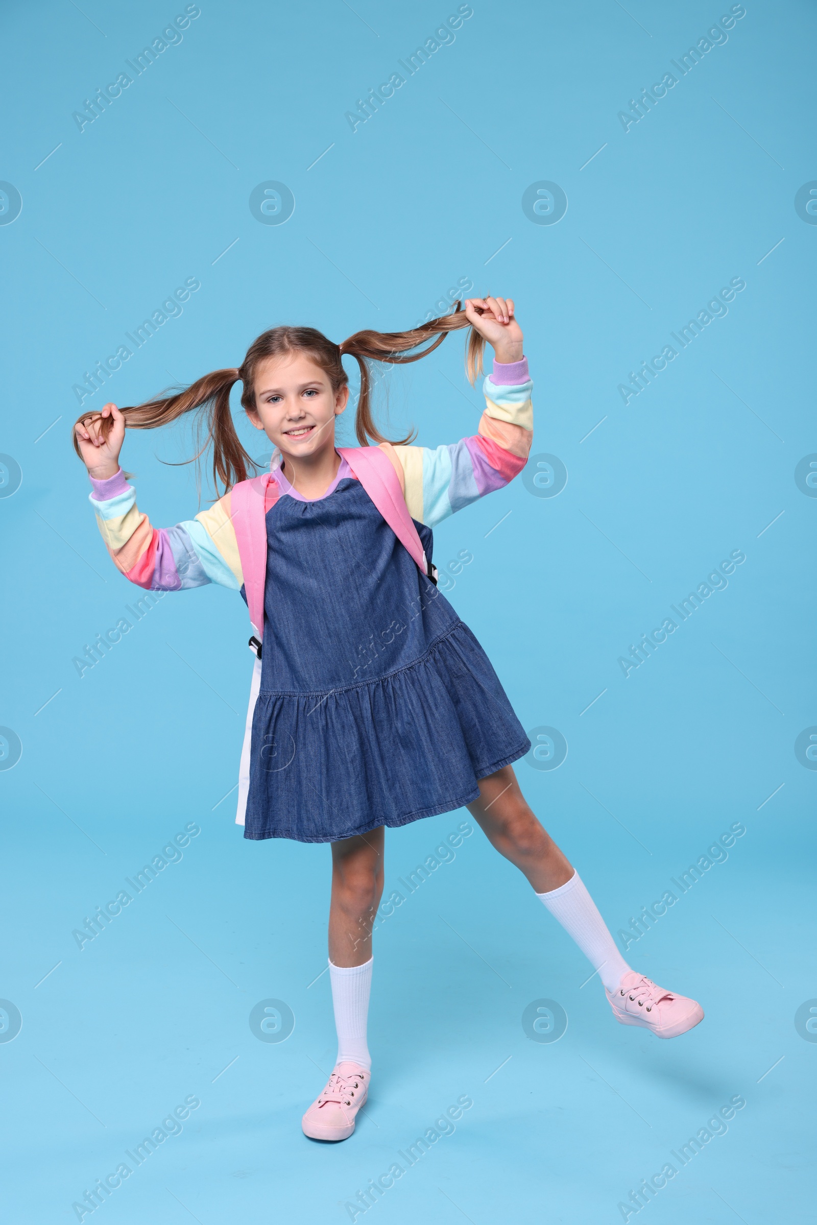 Photo of Happy schoolgirl with backpack on light blue background