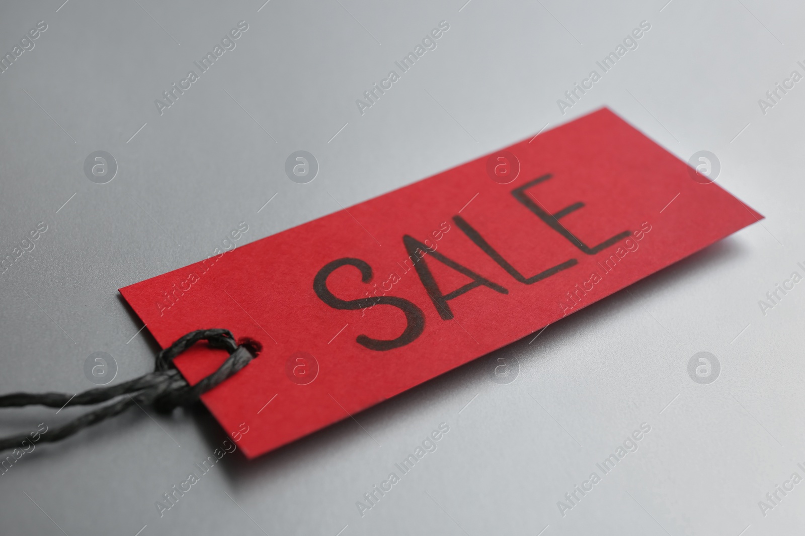 Photo of Red tag with word SALE on light grey background, closeup. Black Friday concept