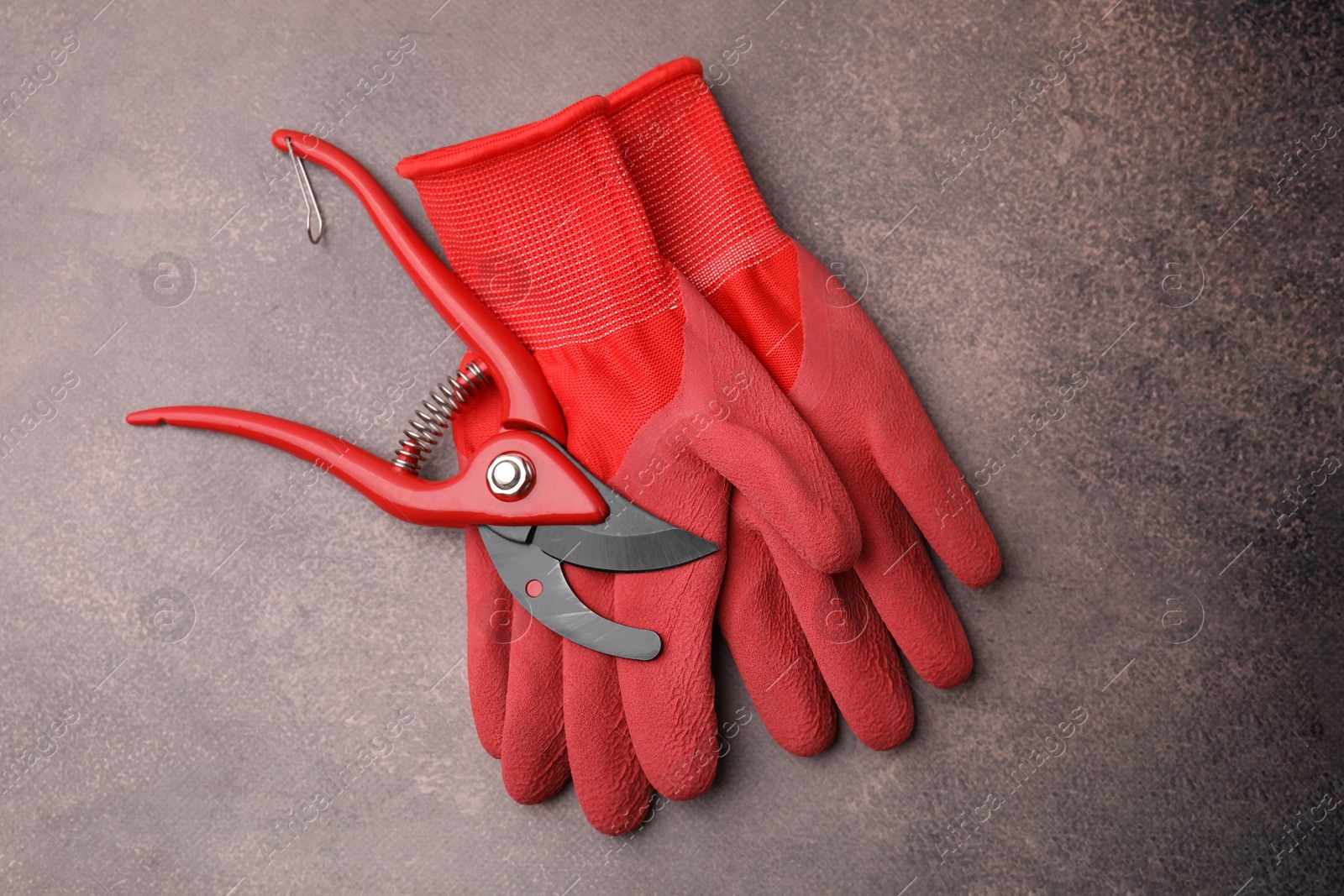 Photo of Pair of red gardening gloves and secateurs on brown textured table, top view