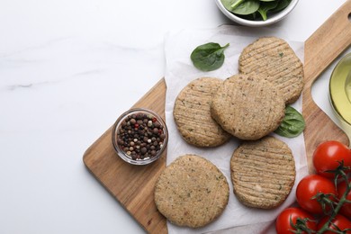 Raw vegan cutlets and different products on white marble table, flat lay