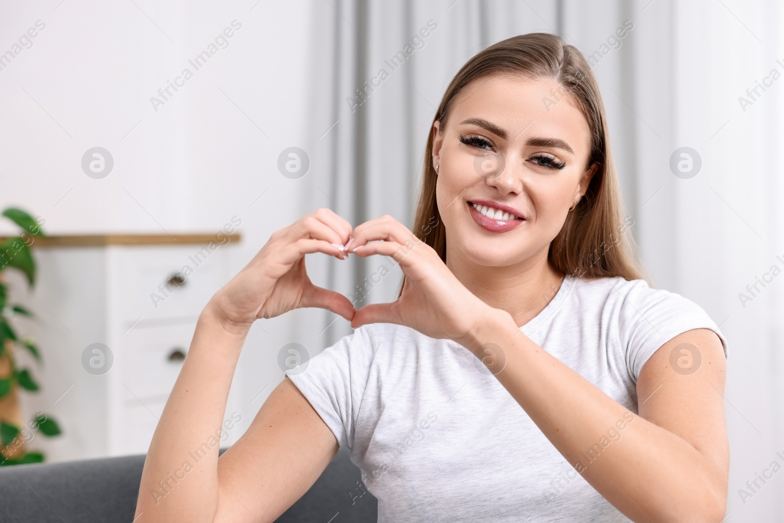 Photo of Happy woman showing heart gesture with hands at home