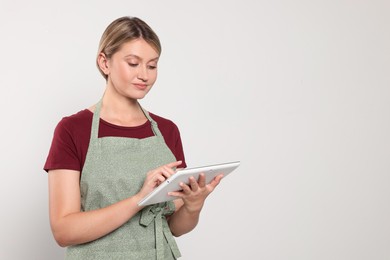 Beautiful young woman in clean apron with tablet on light grey background. Space for text