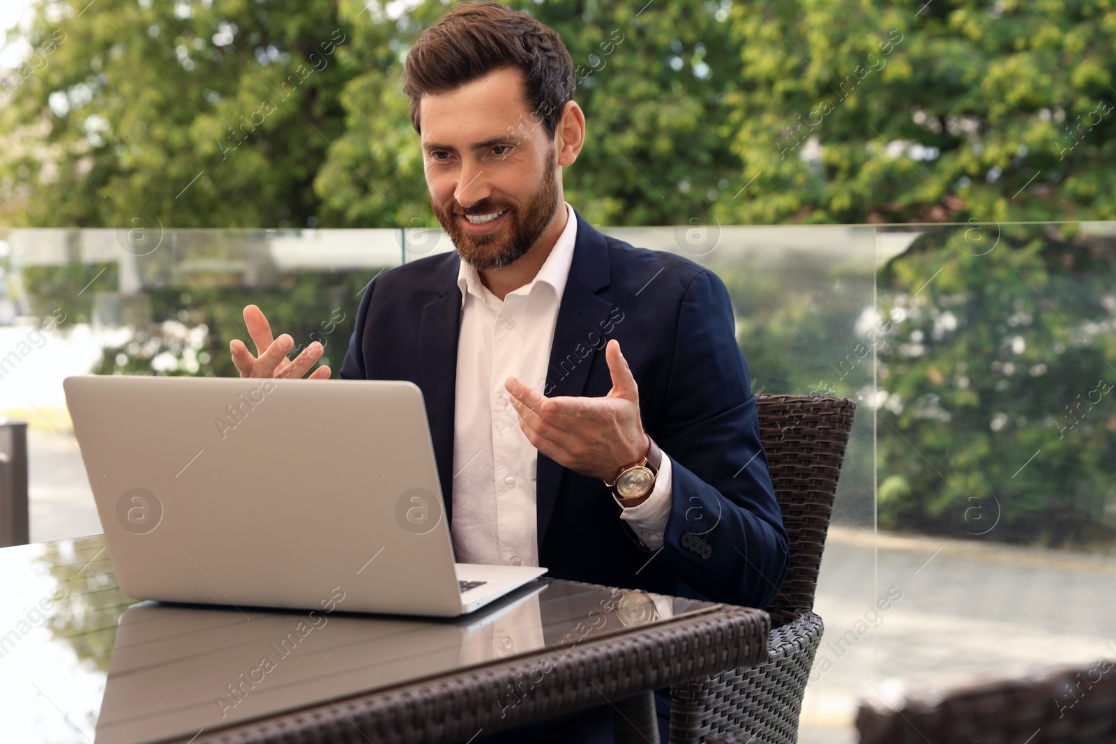 Photo of Happy bearded man having video chat in cafe outdoors