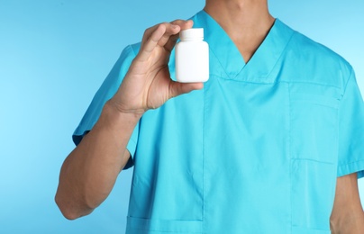 Photo of Male doctor holding pill bottle on color background, closeup with space for text. Medical object
