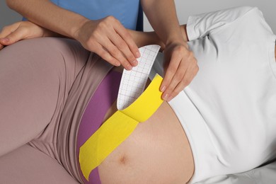 Pregnant woman visiting physiotherapist. Doctor applying kinesio tape, closeup