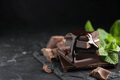 Photo of Tasty chocolate pieces with syrup and mint on black table. Space for text