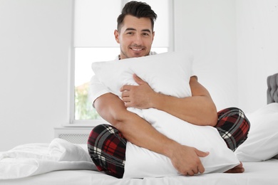 Young man with soft pillow on bed at home