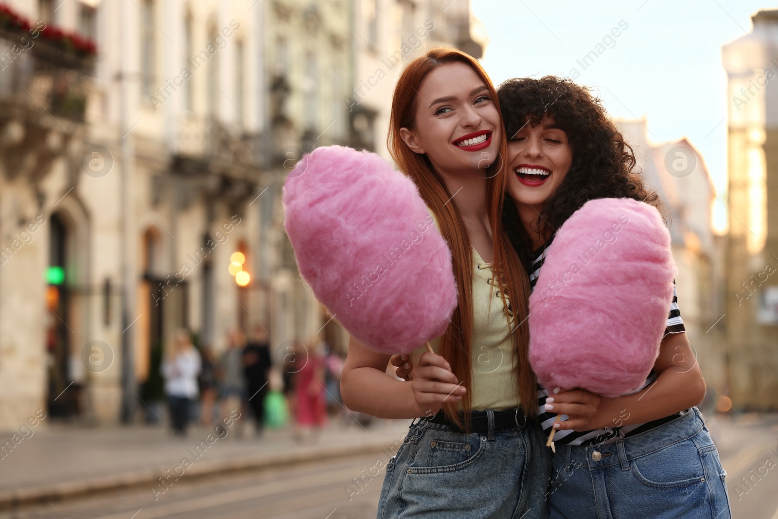 Photo of Happy friends with pink cotton candies on city street. Space for text