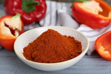 Photo of Bowl with aromatic paprika powder and fresh bell peppers on grey wooden table, closeup