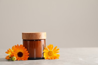 Jar of cosmetic product and beautiful calendula flowers on light grey marble table, space for text